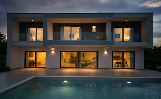 Exterior view of illuminated modern luxury house with swimming pool in foreground at night. Luxury lifestyle concept