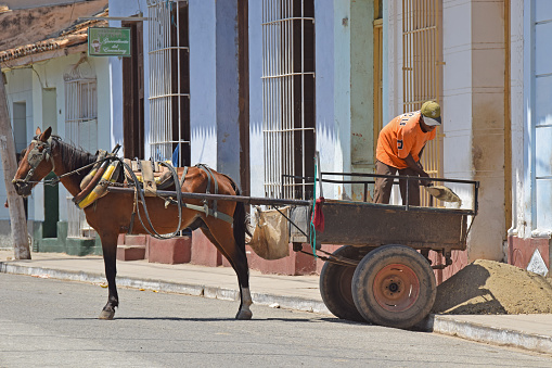 Trinidad, Cuba - April 26, 2016: A man unloads building material from a single-axle horse-drawn cart