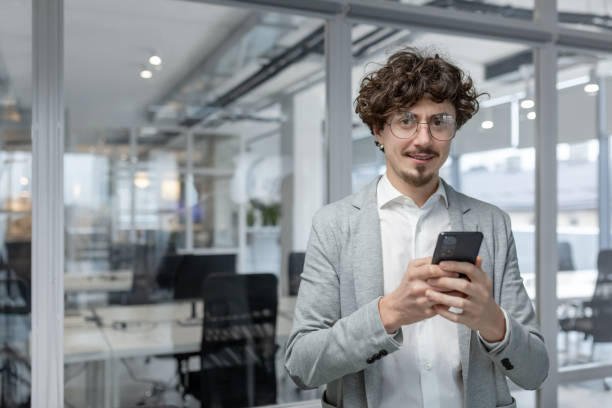 istock Professional young businessman with curly hair using smartphone in modern office space 2035449174