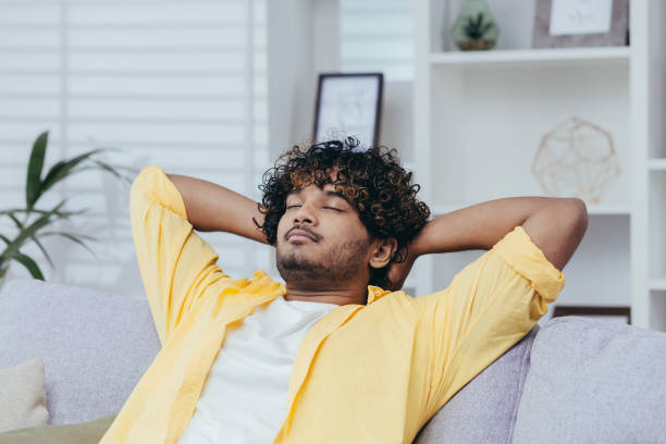 istock Young man relaxing alone at home on sofa, close-up Hispanic man with hands behind head dozing and dreaming with closed eyes in living room of house 2035465188