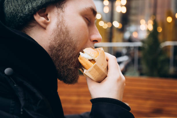 istock A young bearded man eats a burger outside against the backdrop of a cafe. 2035474269