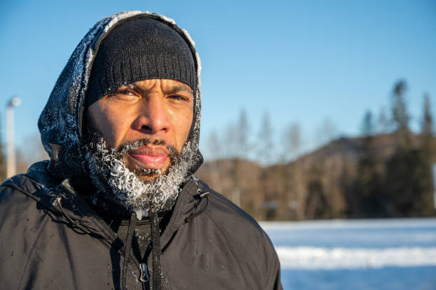 Headshot of black man with frozen beard looking at camera during winter day on clear sky background