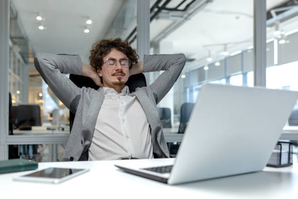 istock Confident young businessman relaxing at office desk with laptop, corporate environment 2035497321