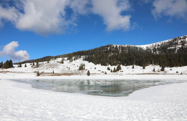 frozen mountain lake in winter with snow and white clouds in the blue sky