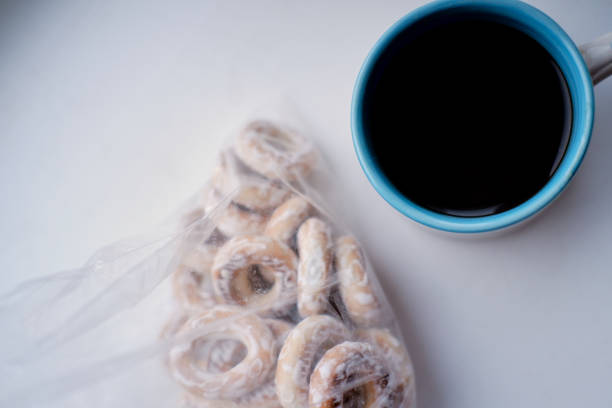 a ceramic cup with black coffee stands on a white table, next to a plastic bag with carbonated bagels