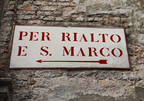 old road sign in the wall in Venice in Italy with text to go at Rialto Bridge or in Saint Mark Square