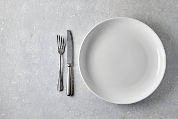 istock White ceramic plate with cutlery on a light stone table. Template for food, top view with copy space 2035526316