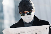 Close-up of a masked reader focused on newspaper.