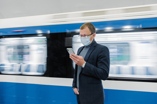 Businessman browsing phone in front of blurred moving train.