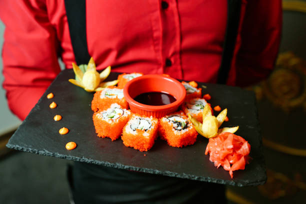A person holds a plate with a variety of sushi rolls.