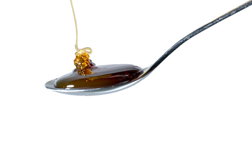Honey flows onto an almost full teaspoon. Isolated on white