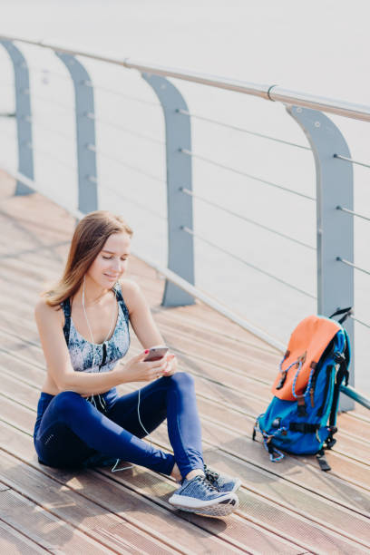 relaxed woman with headphones on a waterfront boardwalk using her cell phone. - cotton swab audio imagens e fotografias de stock