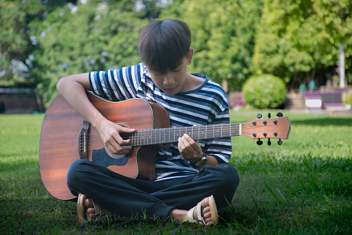 Asian boy spending his freetimes afterschool and on weekend by practising and playing acoustic guitar or ukulele in the backyard of his house.