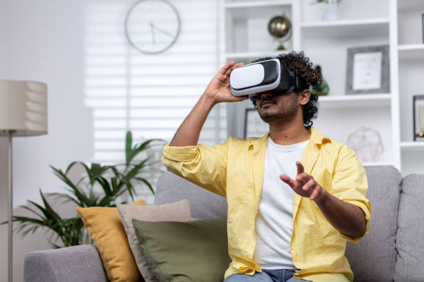 latin american man sitting on couch at home using virtual reality glasses, man viewing educational material remotely - businessman latin american and hispanic ethnicity ecstatic business fotografías e imágenes de stock
