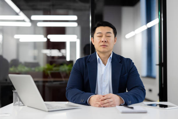 Professional businessman meditating at office desk to reduce work stress