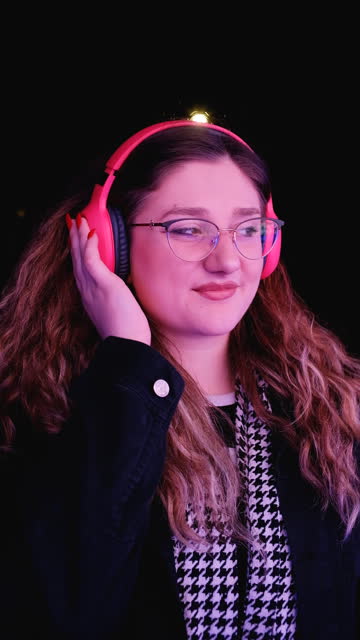 Young woman dancing by the neon lights on the street and listening to music on headphones