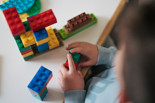 Close-up of little boys building something with plastic blocks on the table.