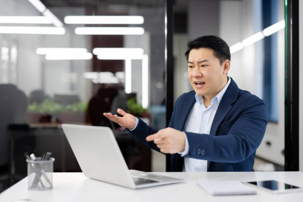 istock Angry angry boss at workplace inside office, senior mature asian man yelling at interlocutor, businessman using laptop for online meeting and remote video call 2035690695