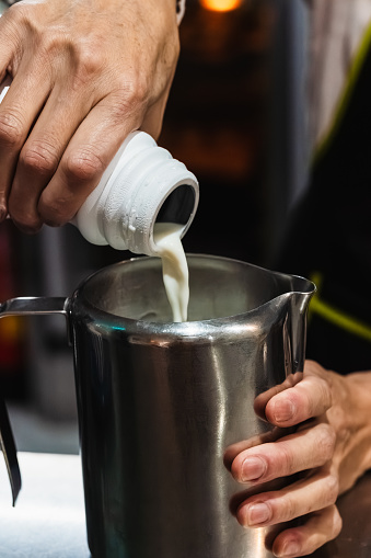 The hands of a Colombian waitress pouring milk into a metal jug to prepare a cappuccino. Service concept.
