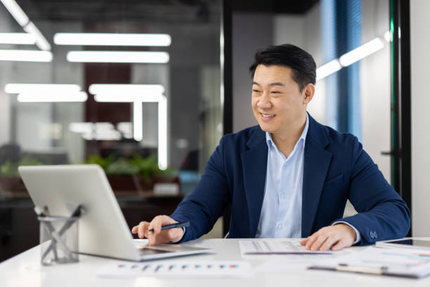 istock Satisfied with achievement male financier accountant inside office at workplace, Asian businessman smiling happy working with accounts contracts and reports, using laptop 2035734342