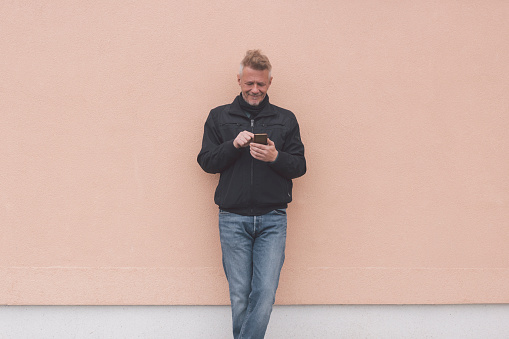 Mature adult leaning on building wall and using phone