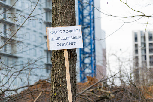 sign in Russian carefully cutting down trees dangerously near a tree against the backdrop of a construction site. concept of cutting down trees during construction. close-up