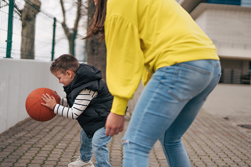 Mother and son play basketball together outdoors.