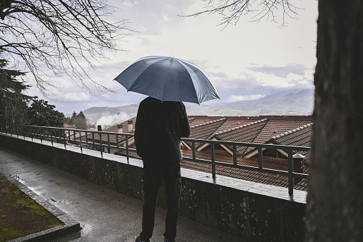 Man in black clothes with umbrella standing on a street and looking at view.