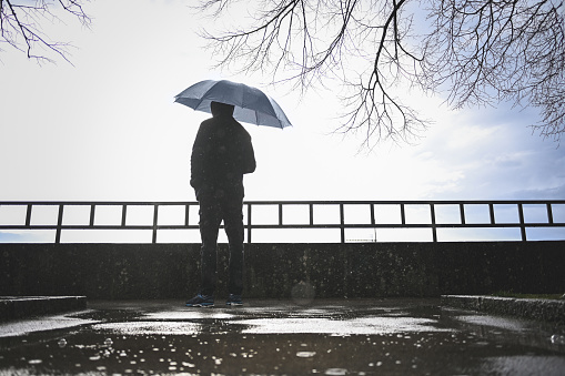 rear view portrait of a man standing under the rain and looking away.