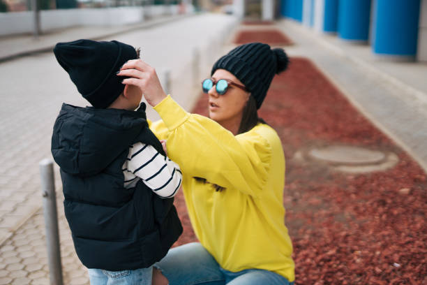 Mother and son spend time outside. A mother puts a cap on her son.