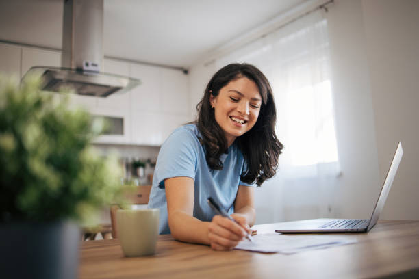 istock A beautiful adult woman is sitting in her kitchen and using a laptop computer. 2035811702