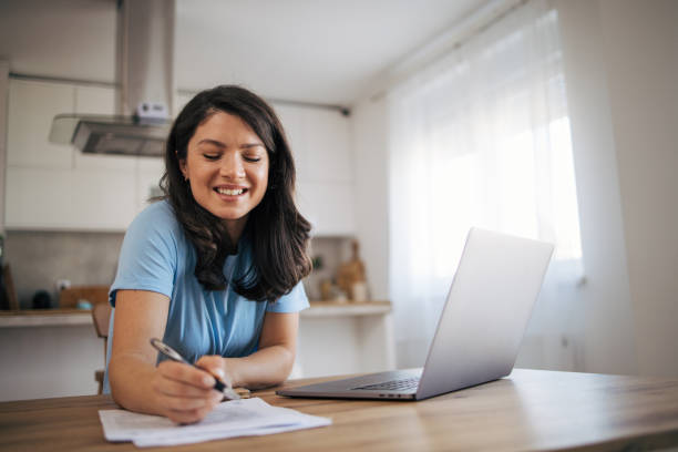 istock A beautiful adult woman is sitting in her kitchen and using a laptop computer. 2035815404