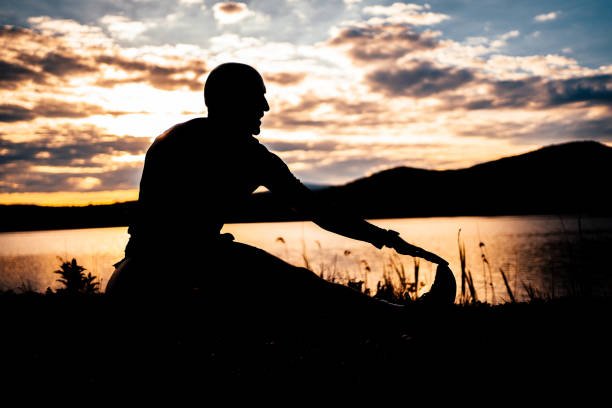 Silhouette of a sporty man doing stretching exercises during sunset