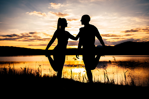 Silhouette of a sporty couple doing stretching exercises by the lake