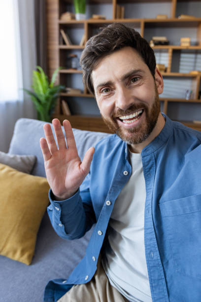 istock Friendly man waving hello in a cozy modern home interior with lively smile 2035845778