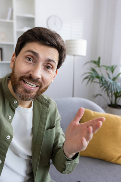 istock Smiling bearded man in casual outfit gesturing while sitting on a sofa at home 2035848399