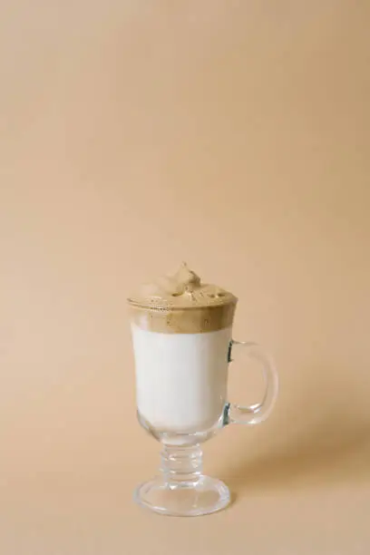 Photo of Beautiful dalgon drink coffee with foam in a transparent mug on a beige background