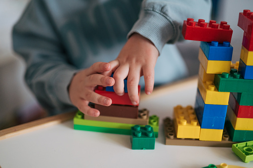 Close-up of little boys building something with plastic blocks on the table.