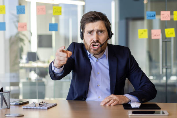 istock Webcam view, angry man with headset phone yelling at webcam, computer screen, businessman arguing with colleagues and partners inside office at workplace, video call online meeting with employees 2035855112