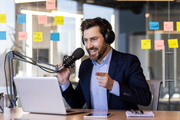 istock A businessman uses a professional microphone inside the office, to record a business training course podcast, a man in a business suit and headphones is happy and smiling at the laptop camera. 2035873204