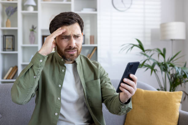 istock Worried mature man with beard using smartphone on home sofa, feeling stressed alone 2035887266