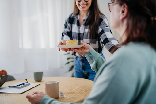 Portrait of a senior woman and her daughter serving a slice of a cake