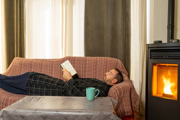 Hispanic man with a beard in his 40s lying on the couch reading a book, he is very comfortable with the heat of a pellet stove.