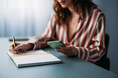 Professional Woman Checking Smartphone at Desk with Notepad and Pen