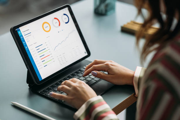 professional woman analyzing data on tablet at work desk - dolu stok fotoğraflar ve resimler