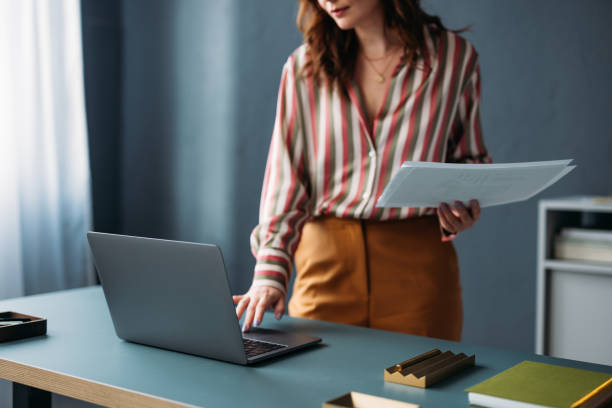 istock Professional Woman Standing at Desk with Laptop and Documents 2035914939