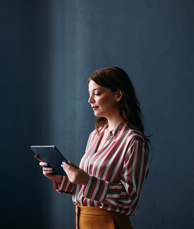 A thoughtful professional woman engages with a tablet, her focused expression suggesting productivity and digital communication.