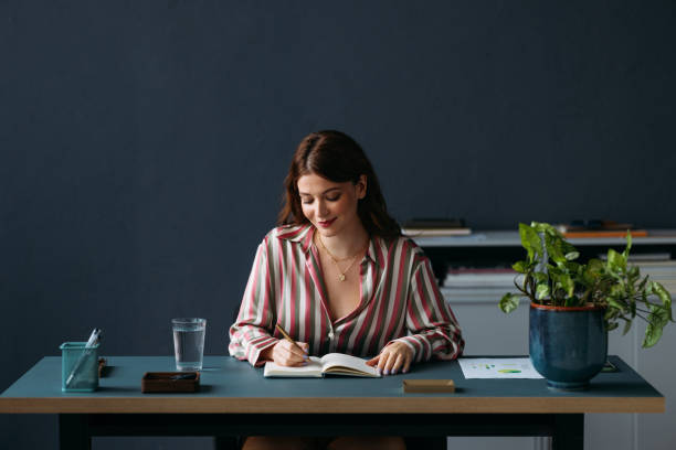 istock Focused Young Woman Writing in Notebook at a Modern Desk 2035915484