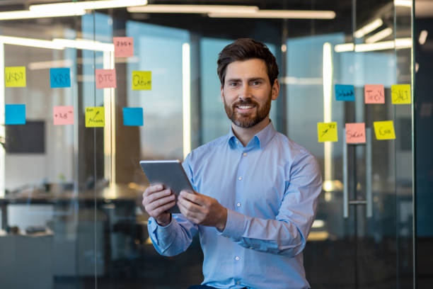 istock Portrait of a smiling young businessman, office center worker and engineering developer standing indoors, holding a tablet and smiling confidently at the camera 2035952811