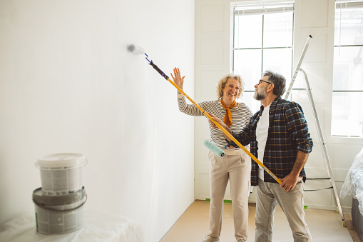 Mature couple painting walls in their apartment, remodeling furniture, and decorating.